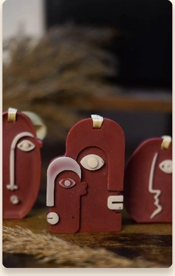 Three maroon sculptural face-charm candles with pale line detailing