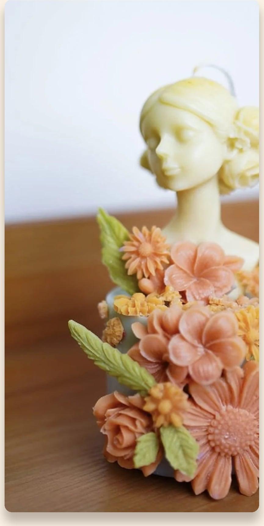 Luma Flora sculpted bust candle crowned with coral and marigold wax blossoms